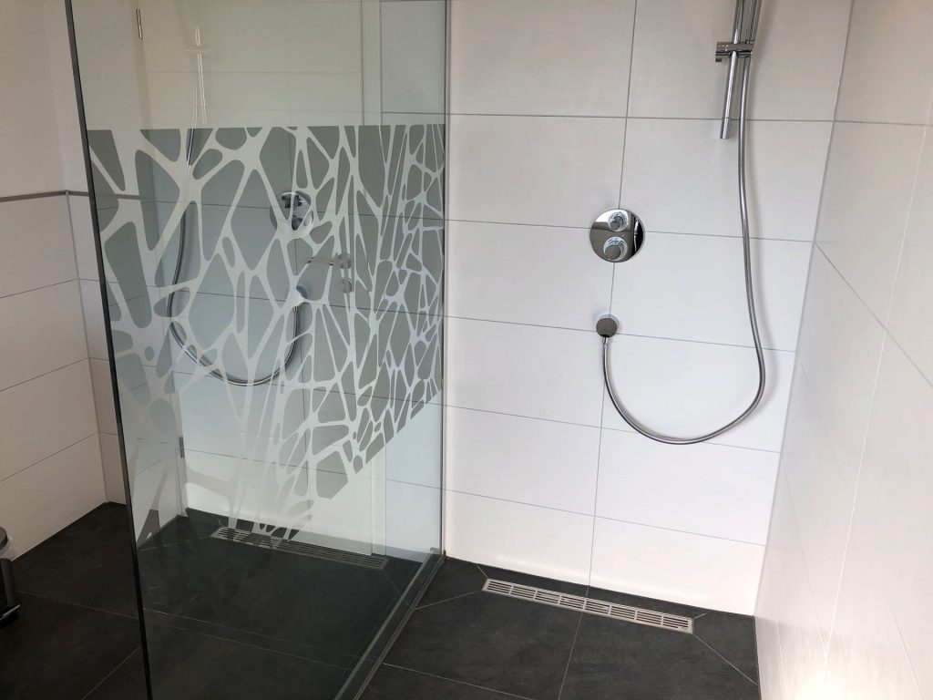 Begehbare Dusche: Barrierefreie Dusche mit Glaswand und grauen Fliesen.