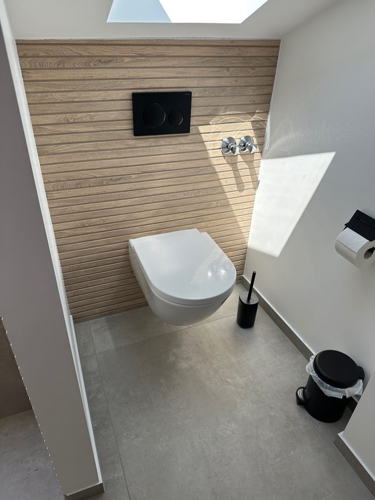 Hänge-WC: Modernes, weißes WC vor einer Wand in Holzoptik.