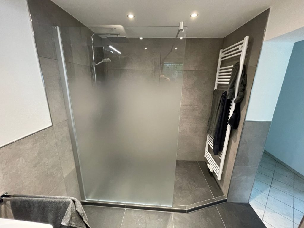 Urinal: Weißes Wand-Urinal in einem hell gefliesten Badezimmer.