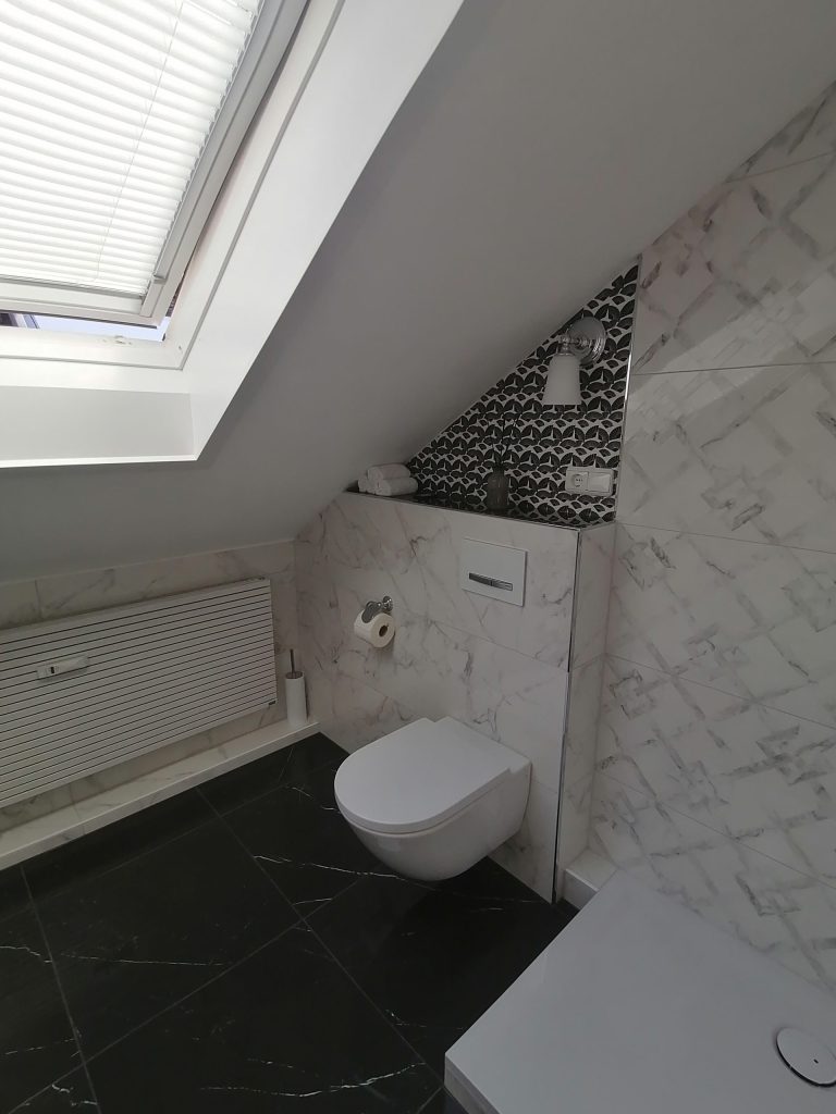 Dachbad: Kompaktes WC unter einer Dachschräge mit kleinem Fenster.