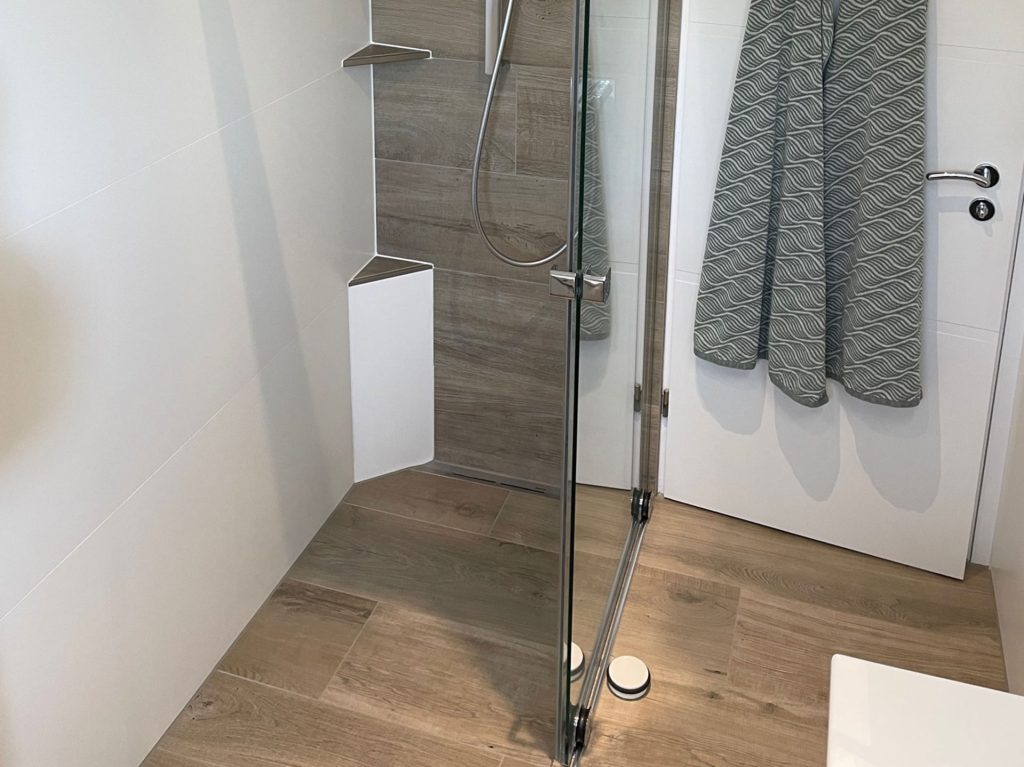 Dusch-Ecke: Dusche mit Glaswand und grauen Wandfliesen.