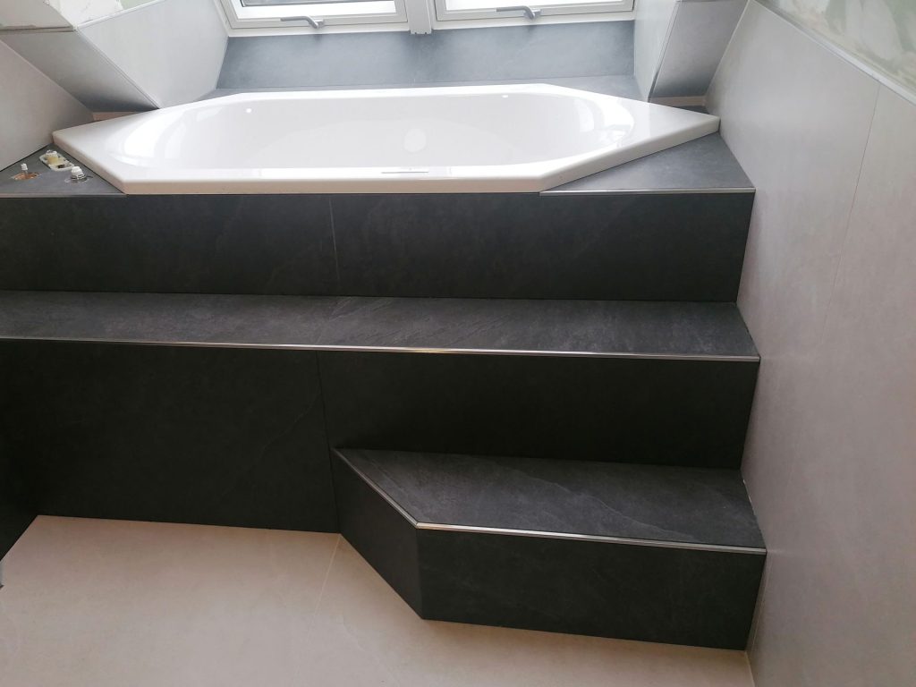 Badewannen-Stufen: Schwarze Treppenstufen, die zu einer Einbaubadewanne führen.
