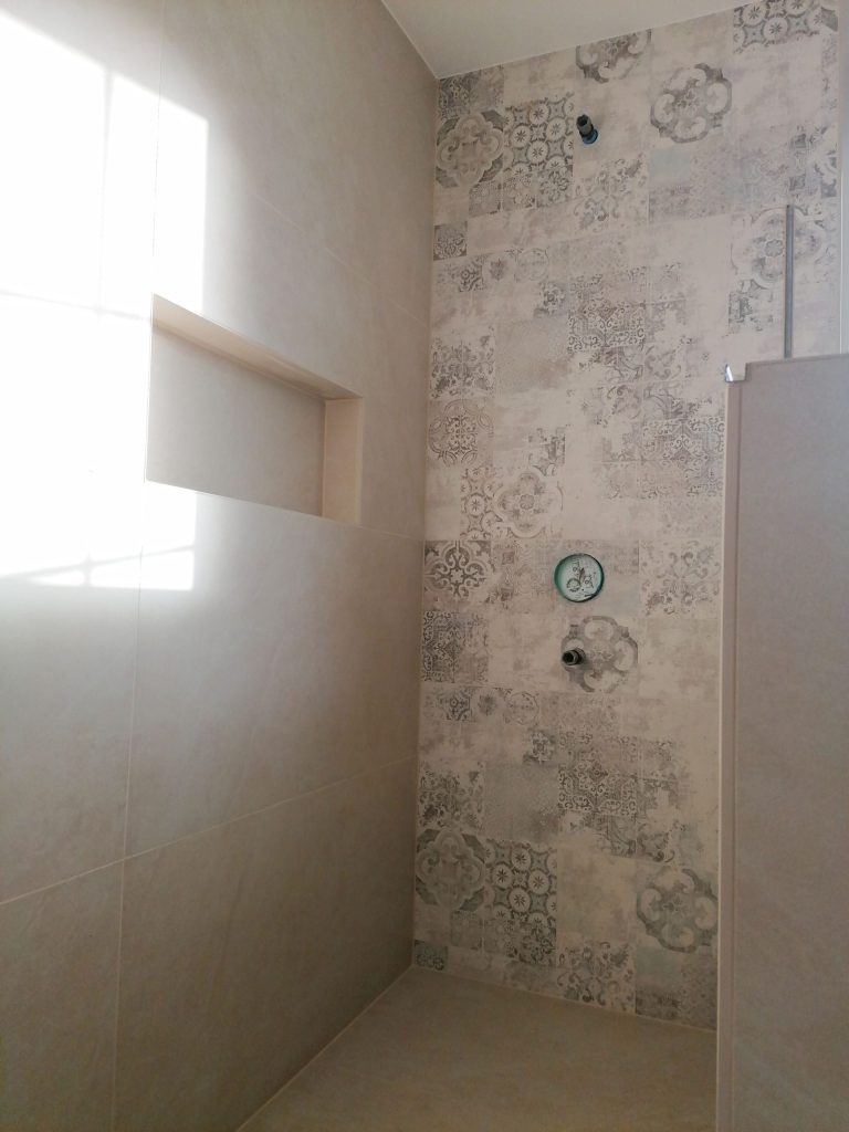Duschnische: Blick in eine Dusche mit gemusterten Fliesen und Deckenbrause.